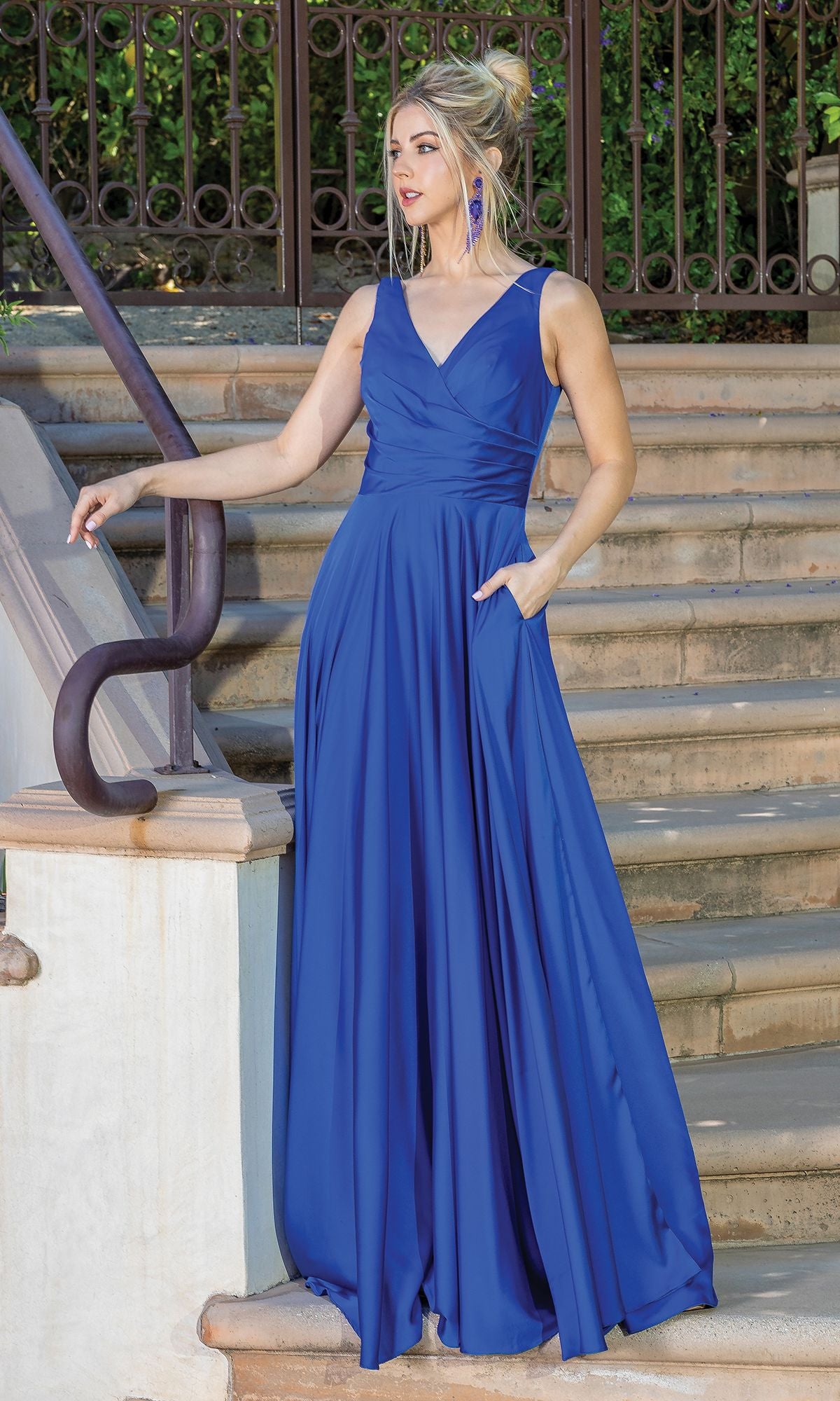 A woman in the Wrap-Bodice Long A-Line Prom Dress with Corset, a sleeveless floor-length royal blue gown under $200, stands on outdoor steps by a metal railing, looking to the side with one hand on her hip.